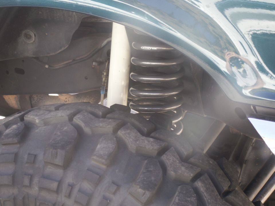 Close-up of a large off-road tire and suspension coil over a dark frame