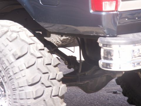 1986 Ford Bronco - The rear suspension and large tire of a dark blue Ford Bronco are visible.