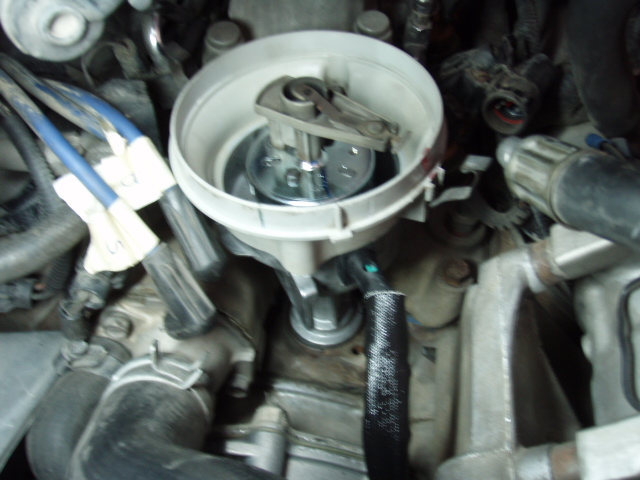 Distributor cap removed, showing rotor and internal components. Wires and engine parts visible