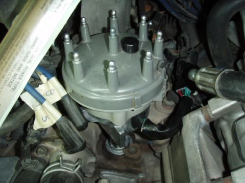 1995 Ford F-150 - Overhead close-up of a gray eight-tower V8 distributor cap installed in an engine bay, with several plug wires removed and new blue wires l…