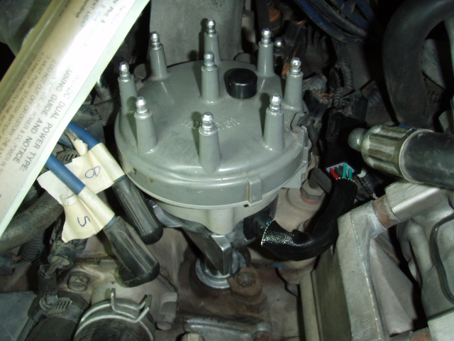 V8 distributor cap in engine bay with numbered masking-tape labels on plug wires