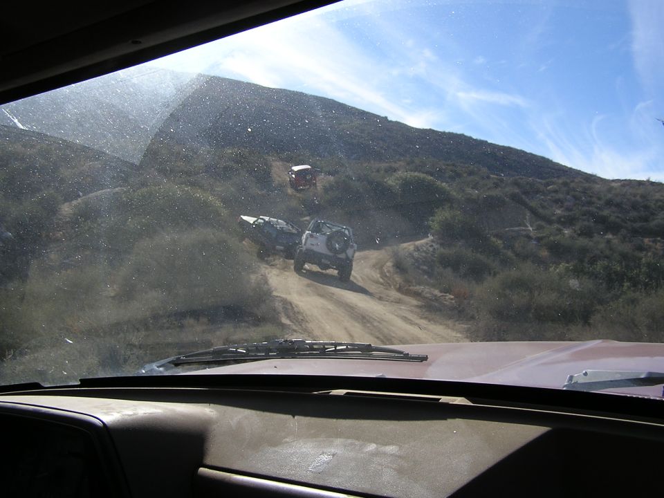 Off-road vehicles climbing a dirt trail seen through a dusty windshield