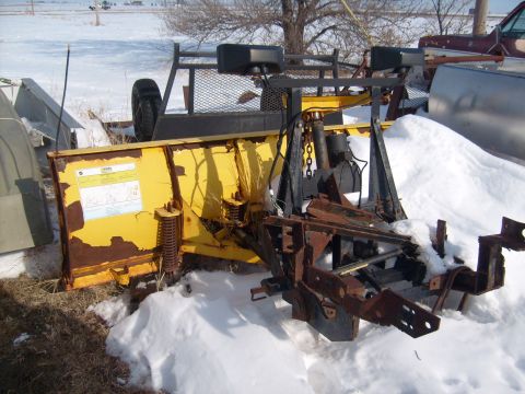1995 Ford C-350 (Centurion Conversions) - A weathered yellow snow plow is partially buried in snow, with visible rust on its metal components.