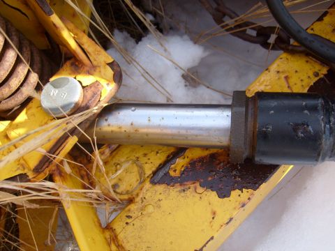 1995 Ford C-350 (Centurion Conversions) - Detail of a plow attachment mechanism, showing a metal pin and bolt against a backdrop of snow and dry vegetation.