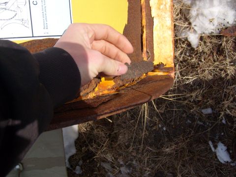 1995 Ford C-350 (Centurion Conversions) - A hand inspects severe rust damage on a yellow metal component, possibly from a plow attachment.