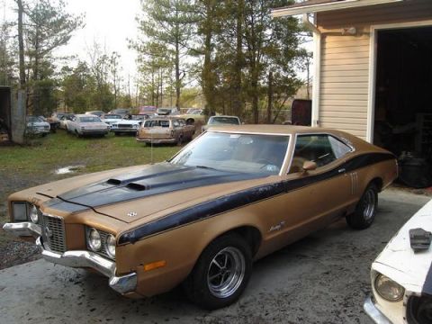 1970 Ford Ranchero - A brown 1970 Ford Ranchero with black racing stripes and hood scoops sits in a yard with other vehicles.