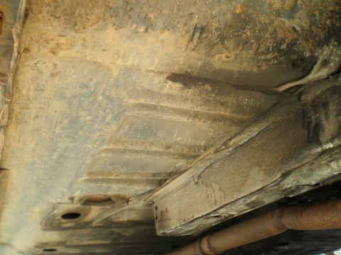 1966 Ford Mustang - The undercarriage of a vehicle displays significant rust and dirt, with visible frame rails and an exhaust pipe.