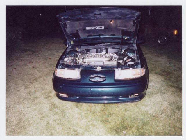 Dark Ford Taurus SHO sedan at night with hood open showing engine and SHO underhood badge
