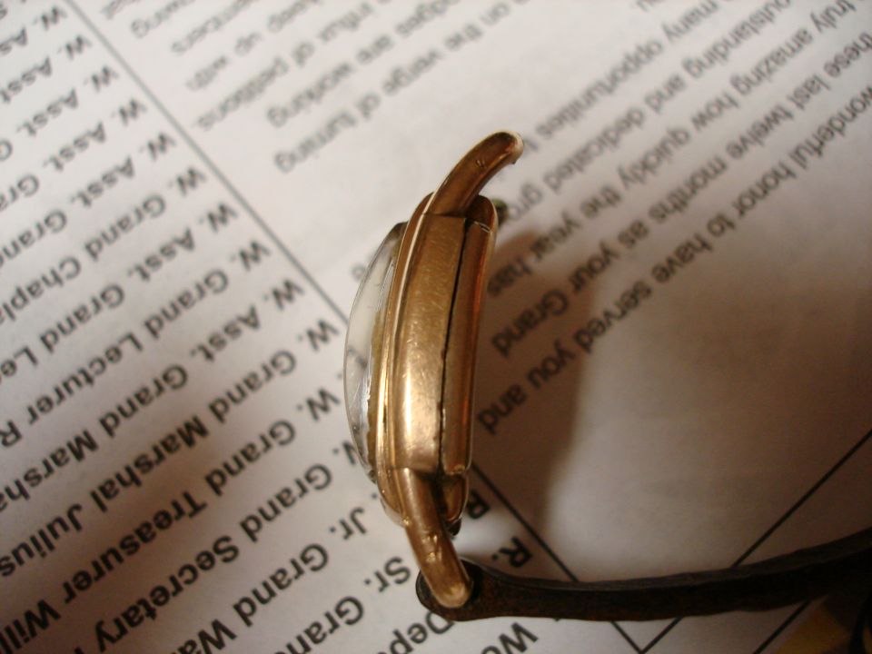 Gold-toned watch case with a cracked crystal, seen from the side against a document