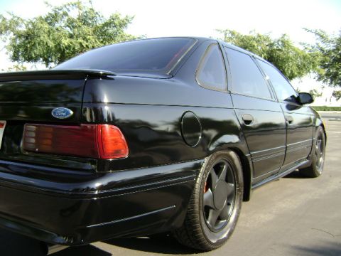 1991 Ford Taurus - Rear quarter view of a black 1991 Ford Taurus sedan with a spoiler and aftermarket wheels.