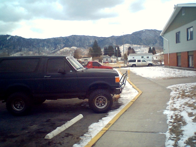 Dark SUV with brush guard parked on a snowy lot, side view
