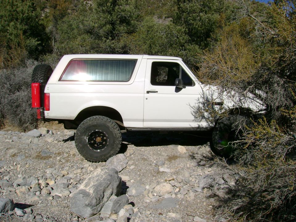 Side view of white lifted Ford Bronco with hardtop and swing-out spare on rocky trail