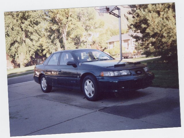 Green Mercury Sable sedan front three-quarter in driveway with black bra, alloy wheels