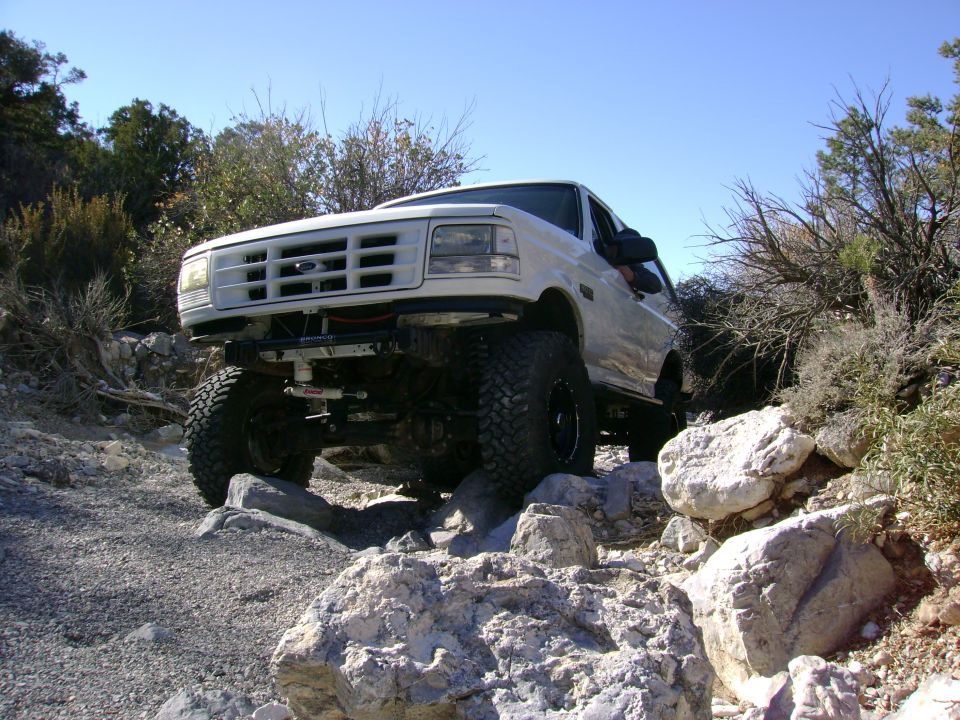 White lifted Ford Bronco climbing limestone rocks, winch and solid front axle visible