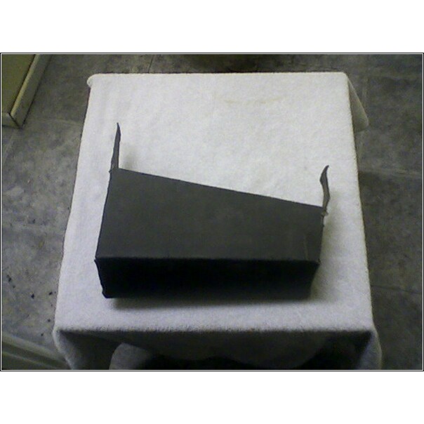 Black plastic part with angled top and two small tabs on the right side, sitting on a white cloth
