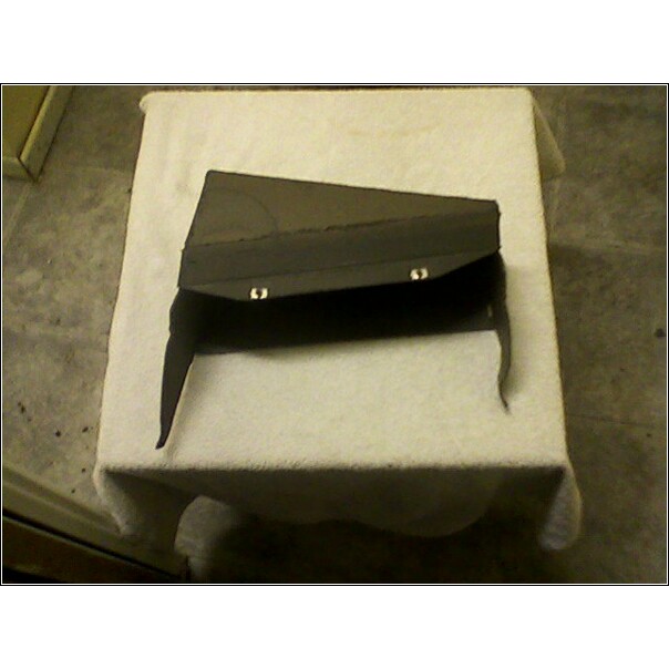 Black car part with two silver clips, resting on a white cloth-covered surface