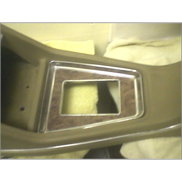 Dashboard trim with wood grain accent and chrome trim around a rectangular opening. The opening reveals yellow foam padding