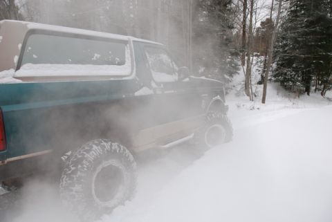 1996 Ford Bronco - A 1996 Ford Bronco drives through a snowy landscape, kicking up a cloud of snow.