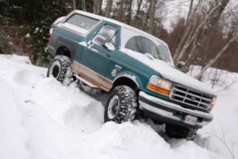 1996 Ford Bronco - A 1996 Ford Bronco navigates a snowy, wooded terrain, with snow covering its body and tires.