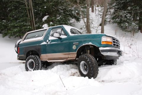 1996 Ford Bronco - A green 1996 Ford Bronco is partially submerged in snow, its lifted suspension and large tires visible.