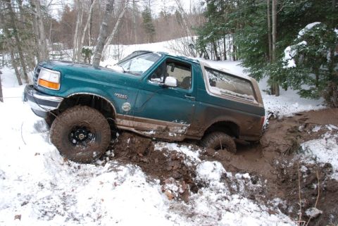 1996 Ford Bronco - A green Ford Bronco is stuck in a muddy, snow-covered ditch during an off-road excursion.
