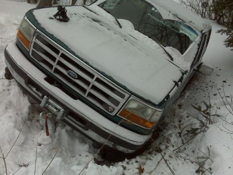 1996 Ford Bronco - A green Ford Bronco is partially buried in snow, with a winch attached to the front bumper.