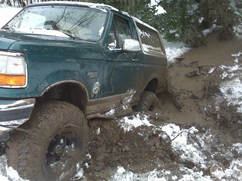 1996 Ford Bronco - A green 1996 Ford Bronco is stuck in a muddy, snowy ditch.