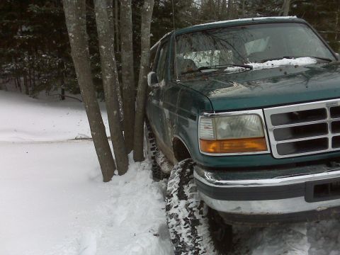 1996 Ford Bronco - A green 1996 Ford Bronco is parked in deep snow next to several trees.