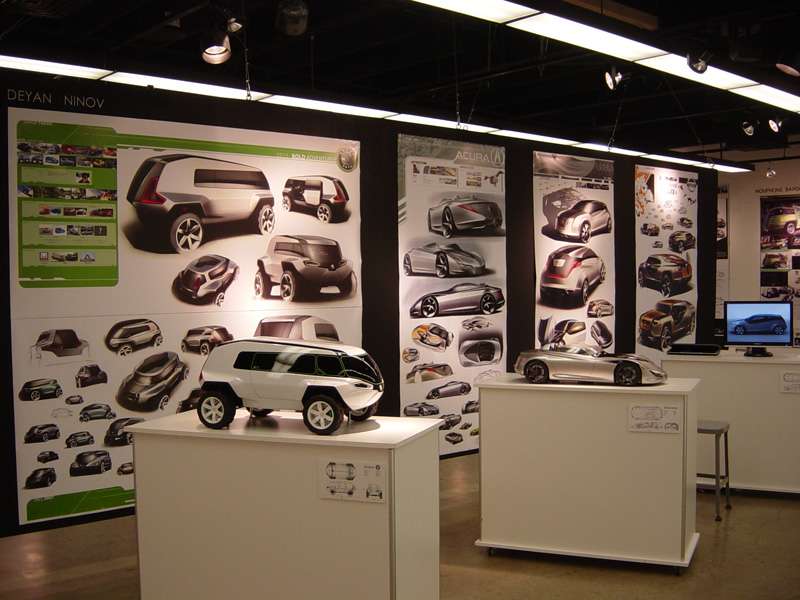 Car design concepts displayed on walls and pedestals, including sketches and models