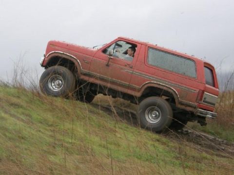 1986 Ford Bronco - A red SUV navigates a muddy incline on an overcast day.
