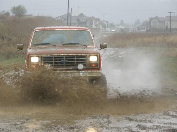 Red Ford Bronco splashing mud, front view, covered in dirt
