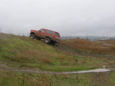 1986 Ford Bronco - Red 1987 Ford Bronco navigates a challenging muddy terrain on an overcast day.