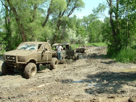 1992 Ford F-350 - Several trucks navigate a challenging muddy path in a wooded area.