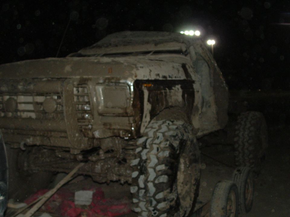Mud-covered truck, front 3/4 view, with large off-road tires and roof-mounted lights