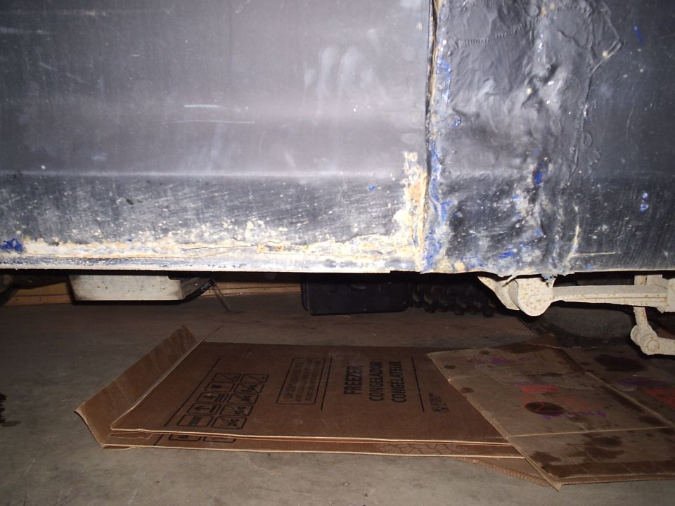 Blue vehicle's rusty lower body panel and undercarriage, with cardboard on the ground