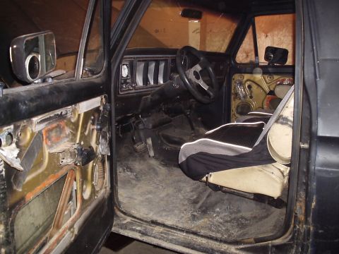 1979 Ford Bronco - The interior of a 1979 Ford Bronco, its dashboard, steering wheel, and worn driver's seat, is visible through the open door.