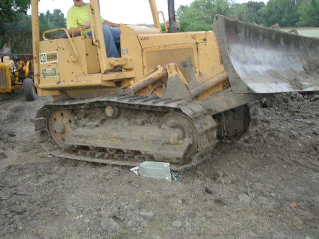 Yellow CAT crawler dozer with raised blade and operator, on muddy ground