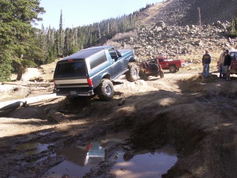 1986 Ford Bronco - Multiple off-road vehicles, including a 1986 Ford Bronco, tackle a challenging muddy course.