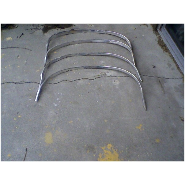 Four curved chrome trim pieces with visible wear, lying on a cracked concrete floor