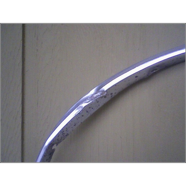 Chrome trim piece with dents and rust spots against a wood-paneled background