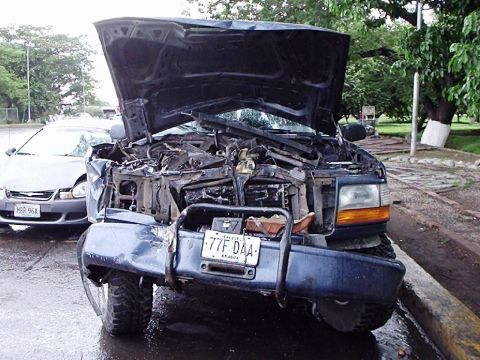 1995 Ford F-150 - A severely damaged 1995 Ford F-150 pickup truck sits on a curb after an accident, with its hood open revealing extensive front-end damage.