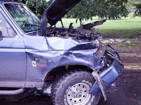 1995 Ford F-150 - A heavily damaged blue 1995 Ford F-150 sits with its hood open after an accident.