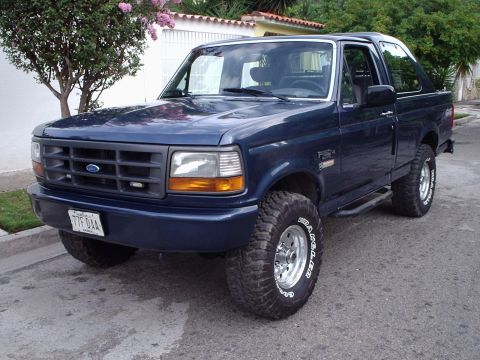 1995 Ford F-150 - This blue Ford Bronco is parked on a residential street. The vehicle has a removable top.