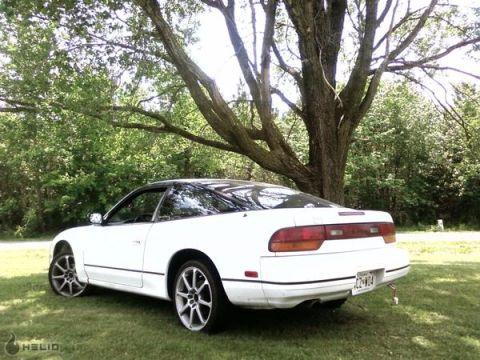 1991 Nissan 240SX - A white coupe with a black roof is parked on a grassy lawn under a large tree.