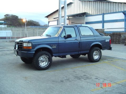 1995 Ford F-150 - Blue Ford Bronco with aftermarket wheels and tires parked outdoors.