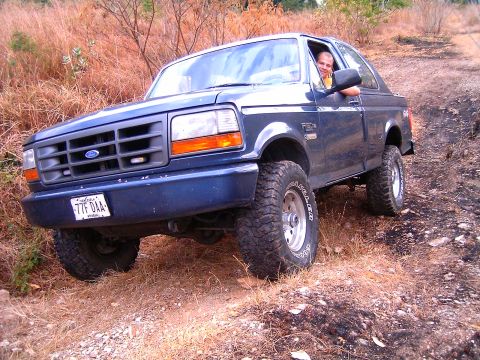 1995 Ford F-150 - A blue Ford Bronco navigates an off-road trail, its lifted suspension and tires.
