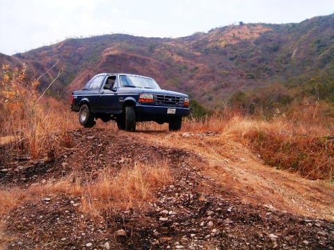 1995 Ford F-150 - A dark blue pickup truck is parked on a dirt hill with dry grass and mountains in the background.