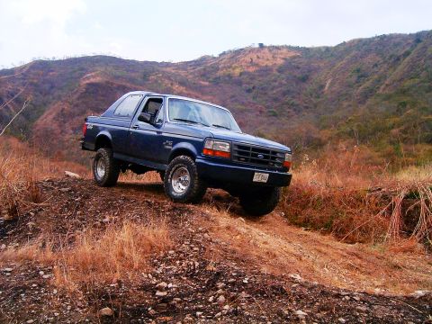 1995 Ford F-150 - A blue Ford Bronco navigates a dry, hilly terrain with sparse vegetation.