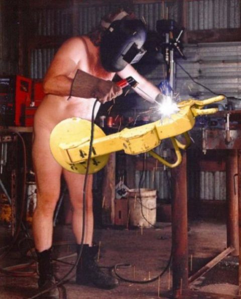 1994 Ford Bronco - A man in a welding mask and boots works on a yellow robotic arm in a workshop.