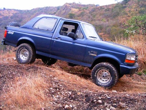1995 Ford F-150 - This blue Ford Bronco is navigating a rough, dry, grassy hillside.
